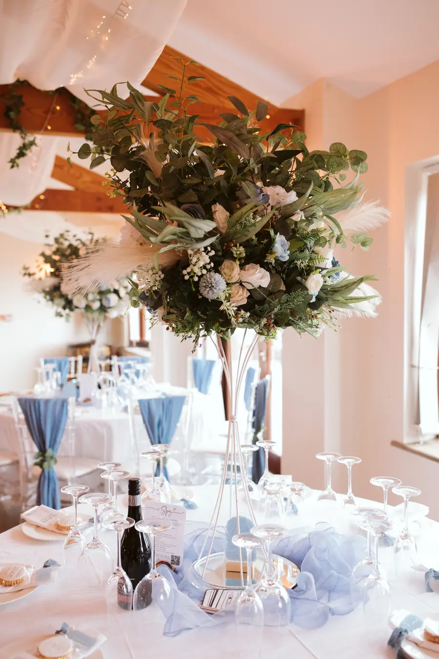 White flowers and greenery rising above clear glasses on a dinner table