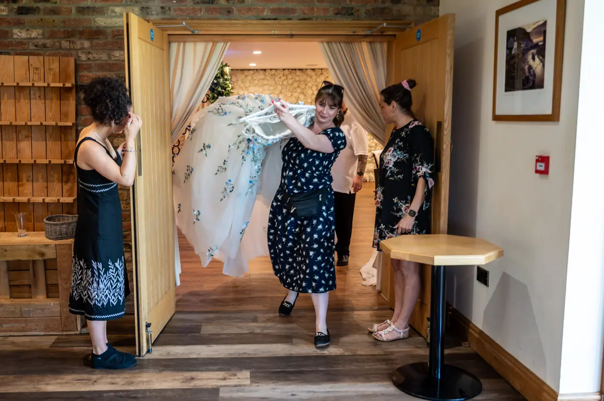 Woman carrying Megan's floral wedding dress into the preparation room
