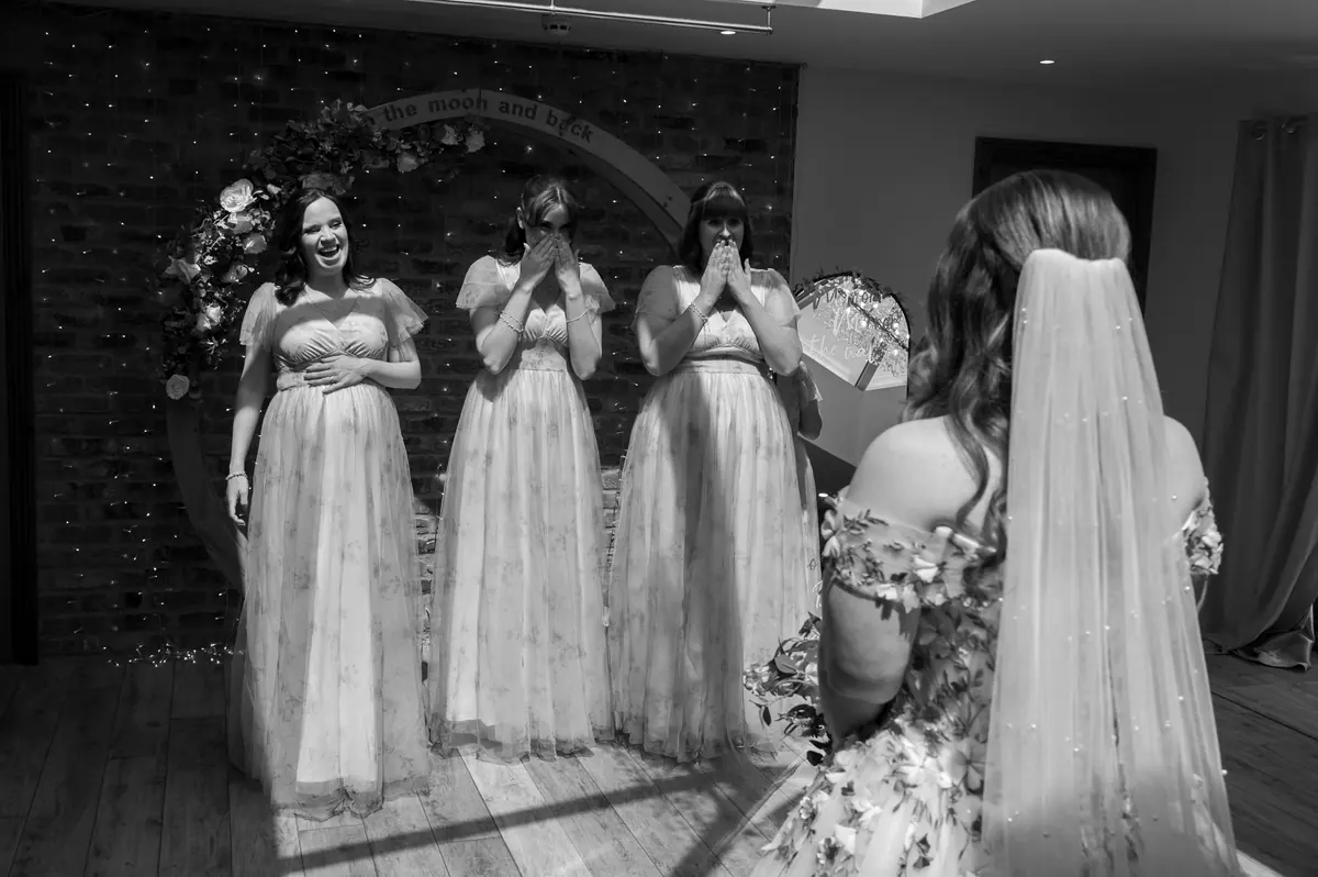 Four women in pale blue dresses facing Megan in black and white