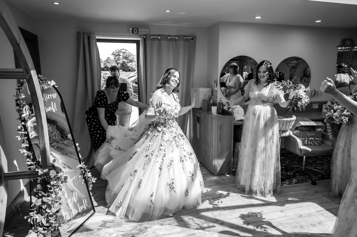 Women adjusting Megan's floral gown beside the round mirrors in monochrome