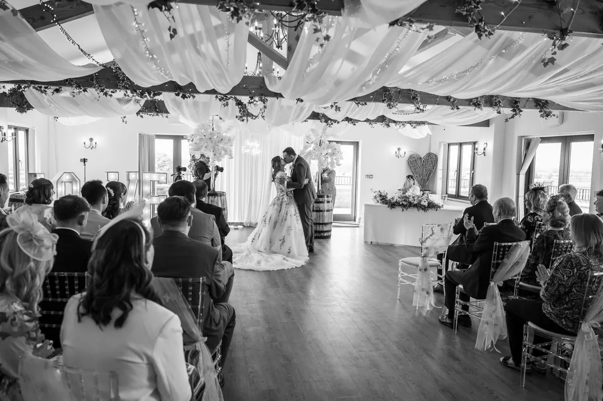 Megan and Dan beneath the wooden ceremony arch in monochrome