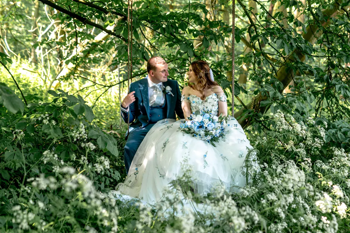 Megan and Dan seated together among white flowers beneath leafy trees