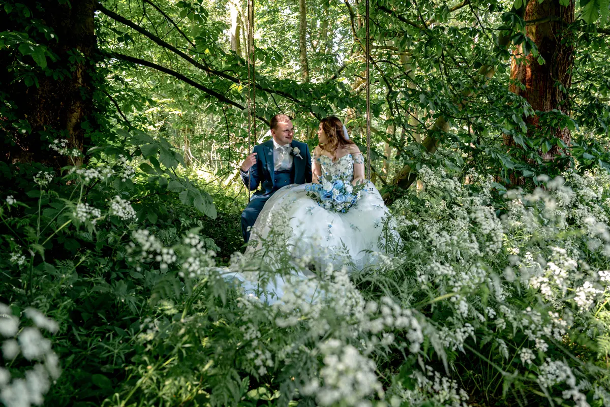 The couple seated among white flowers under dense woodland branches
