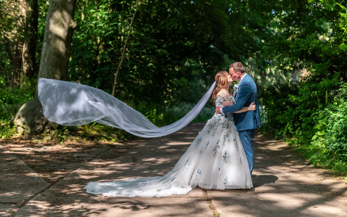 The couple kissing beneath a wide veil on the wooded lane