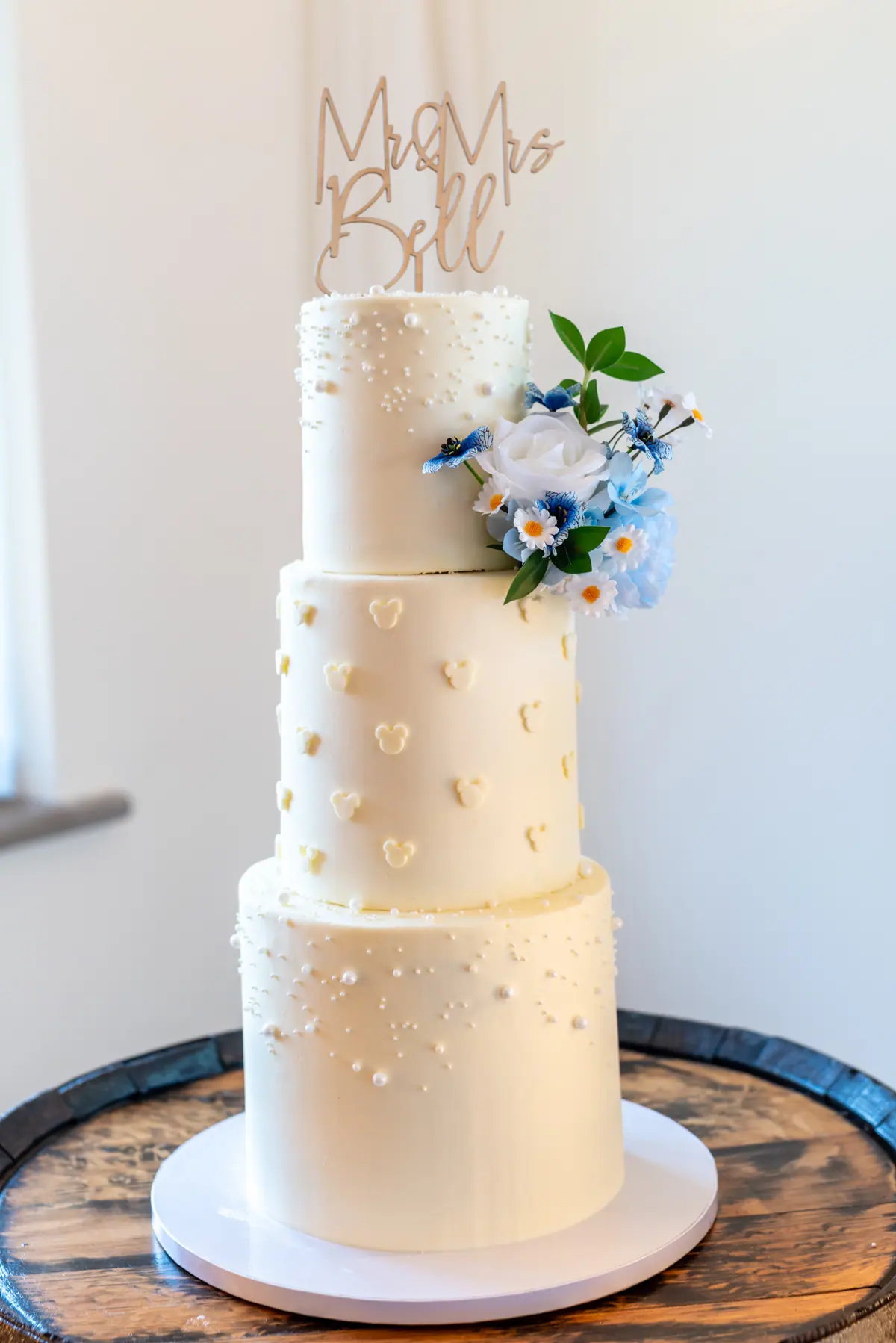 White wedding cake with blue flowers displayed on a wooden barrel