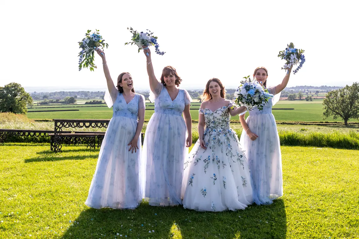 Four women raising blue and white bouquets against the open fields