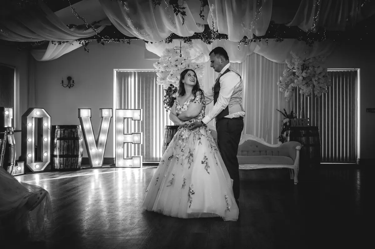Megan and Dan dancing beside illuminated LOVE letters in monochrome