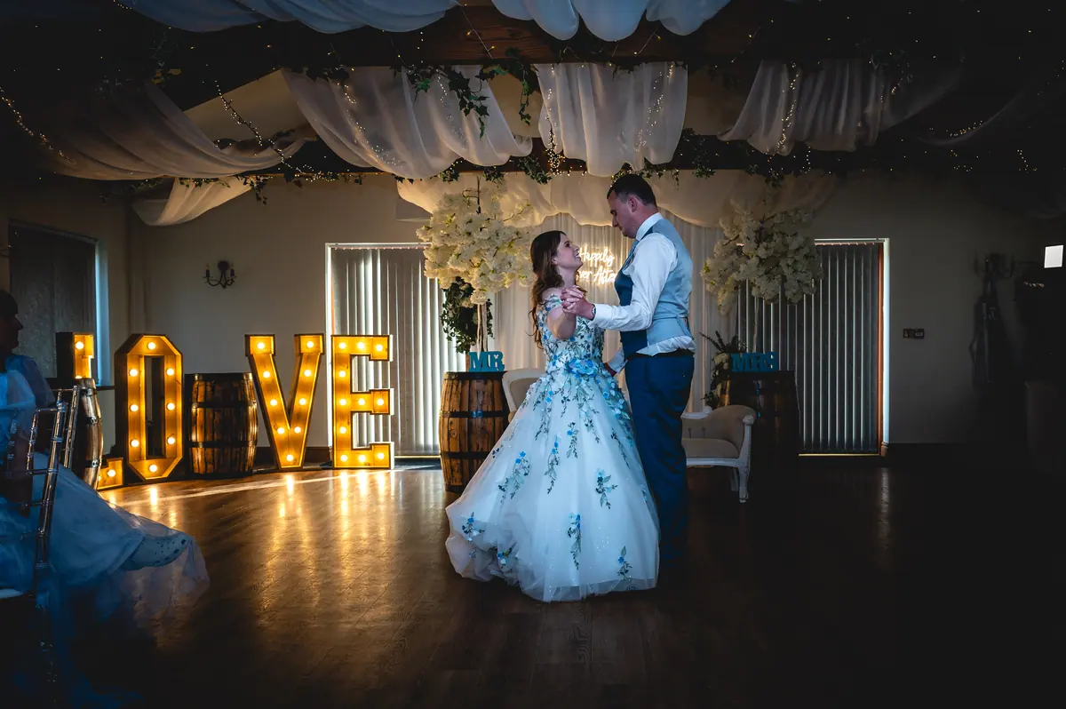 The couple dancing beside glowing LOVE letters inside the darkened Hall