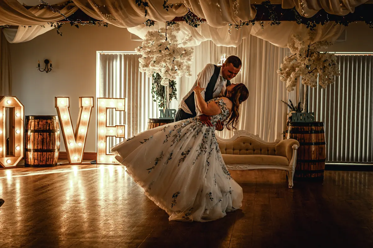 Dan dipping Megan beside glowing LOVE letters and wooden barrels