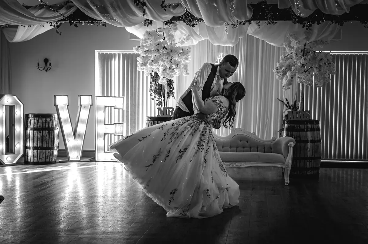 The couple dancing beside LOVE letters in a wide monochrome view