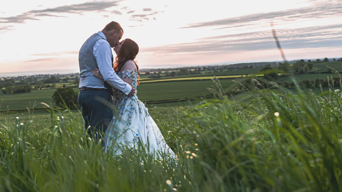 Megan and Dan standing close together in long grass near sunset