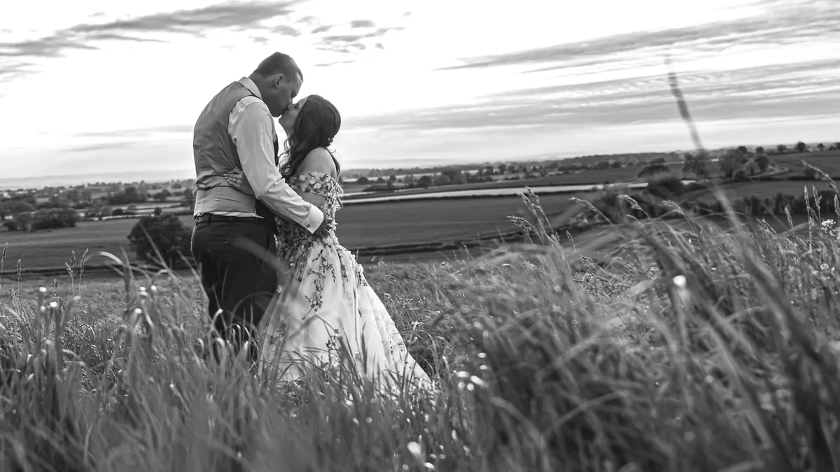 The couple embracing in long grass in a black and white view