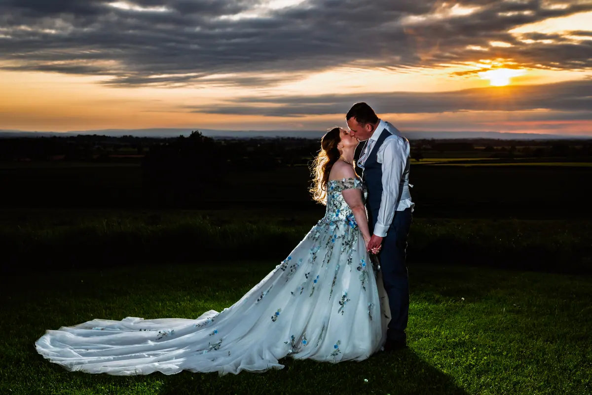 The couple kissing on the grass beneath a dark orange sky