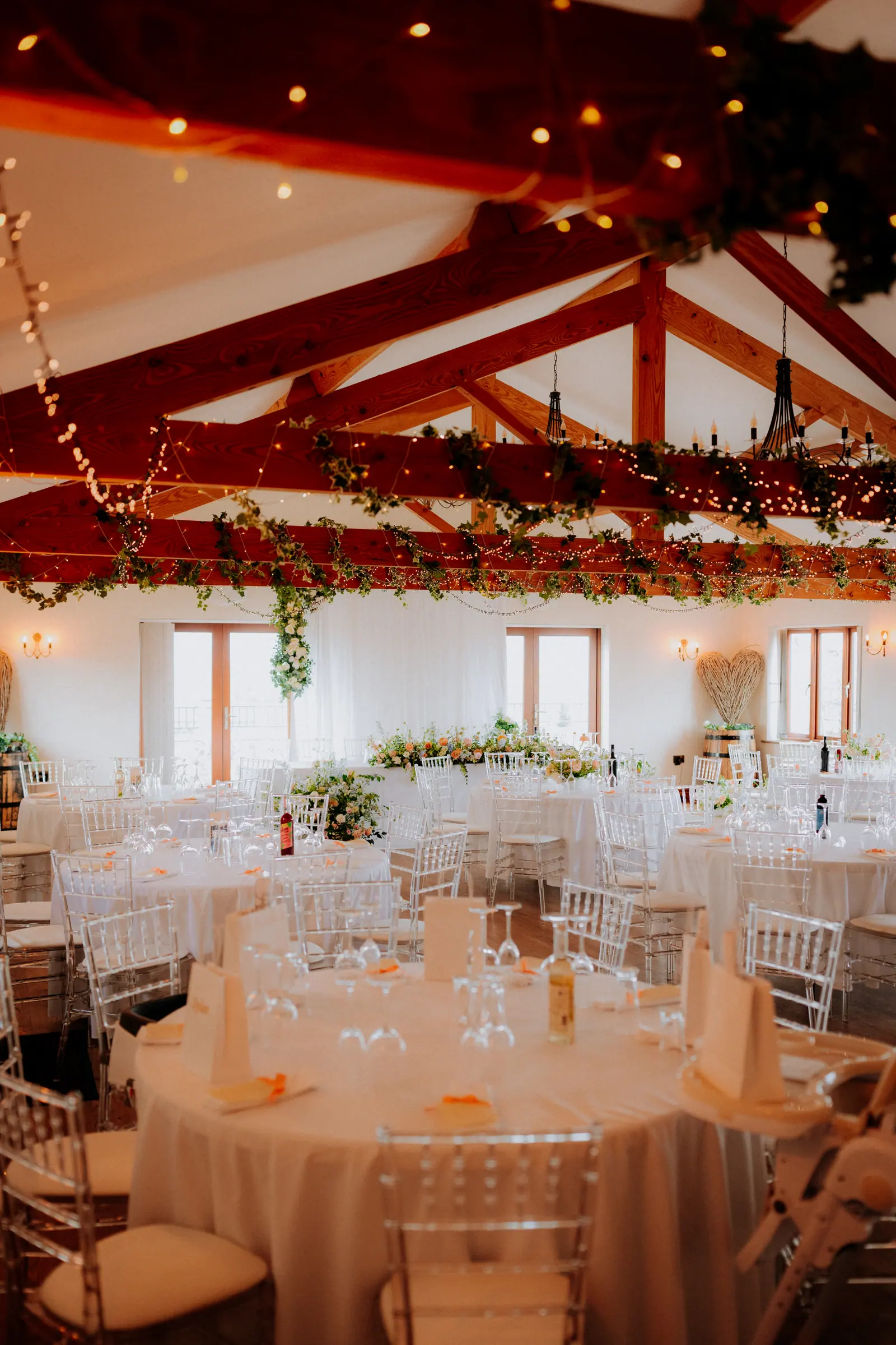 Round Hall tables dressed beneath greenery, white fabric and warm lights