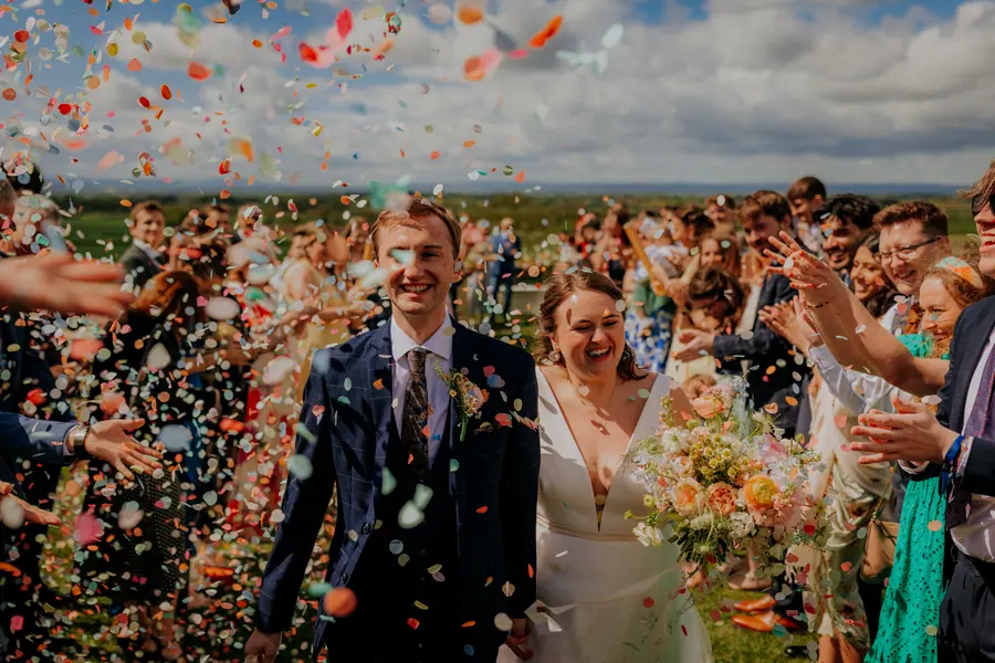 Megan and Patrick walking through a dense shower of coloured confetti