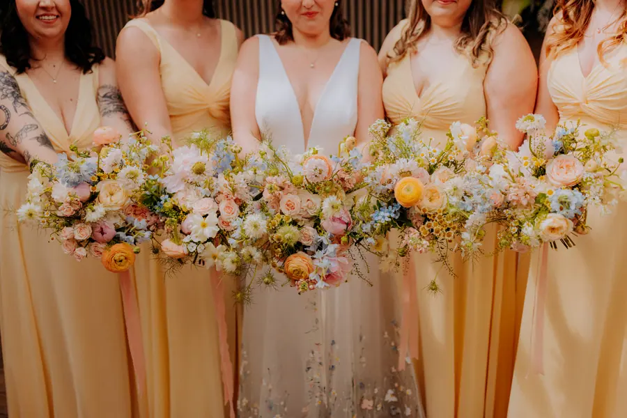 Women in pale dresses holding matching peach and white flower bouquets