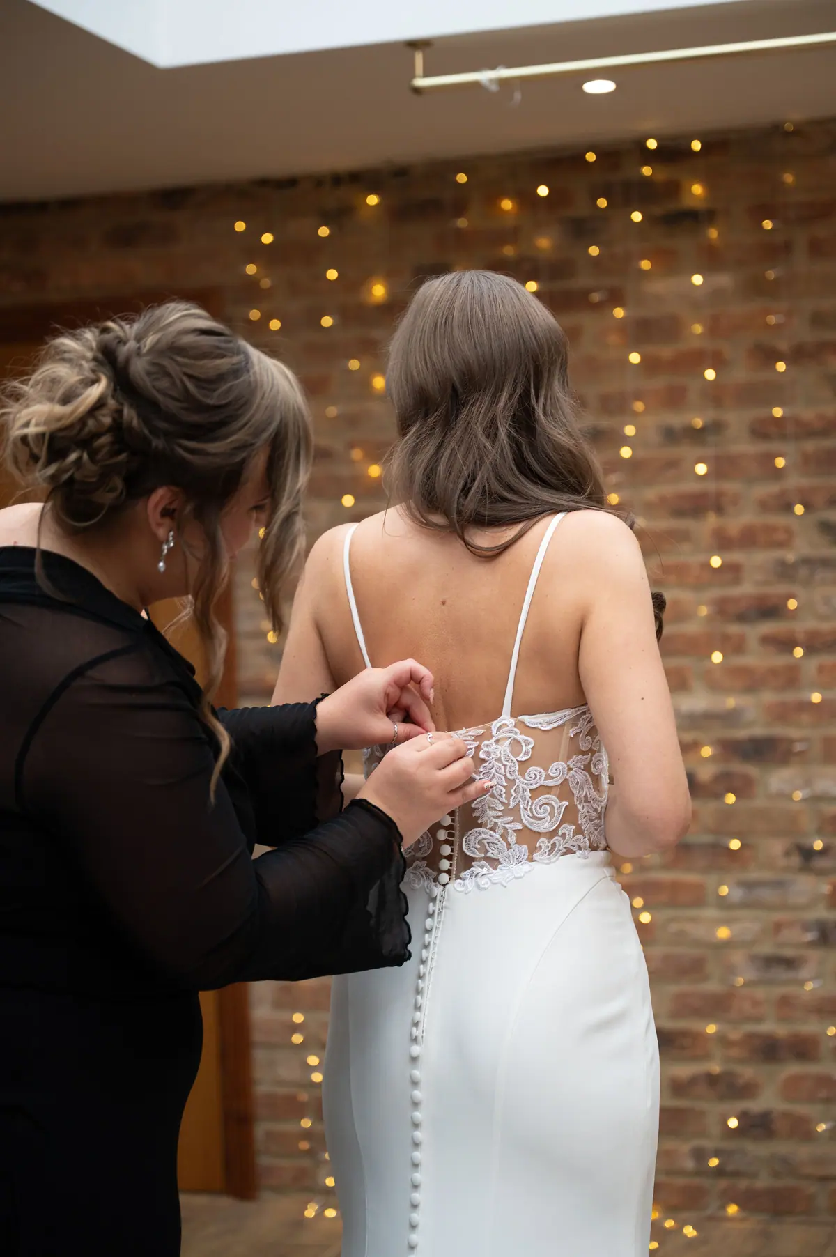 Woman fastening the back of Natalie's white dress against brick walls