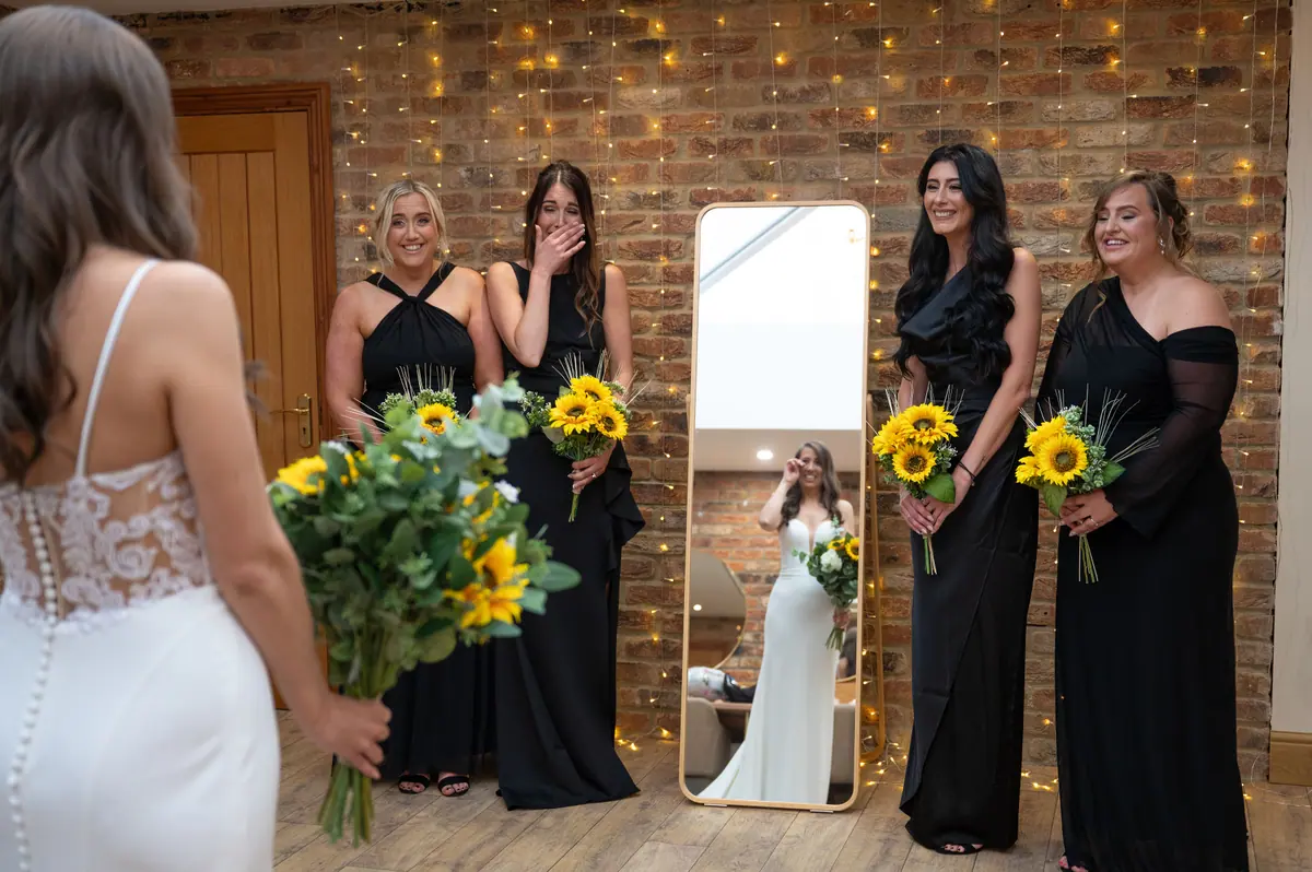 Natalie facing women in black dresses carrying bright sunflower bouquets
