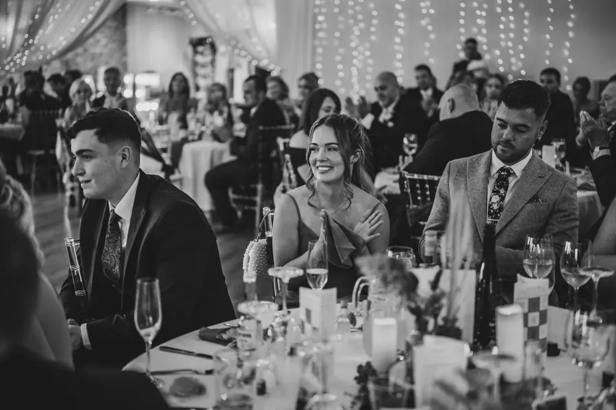 Guests seated during a speech as the couple listen in black and white