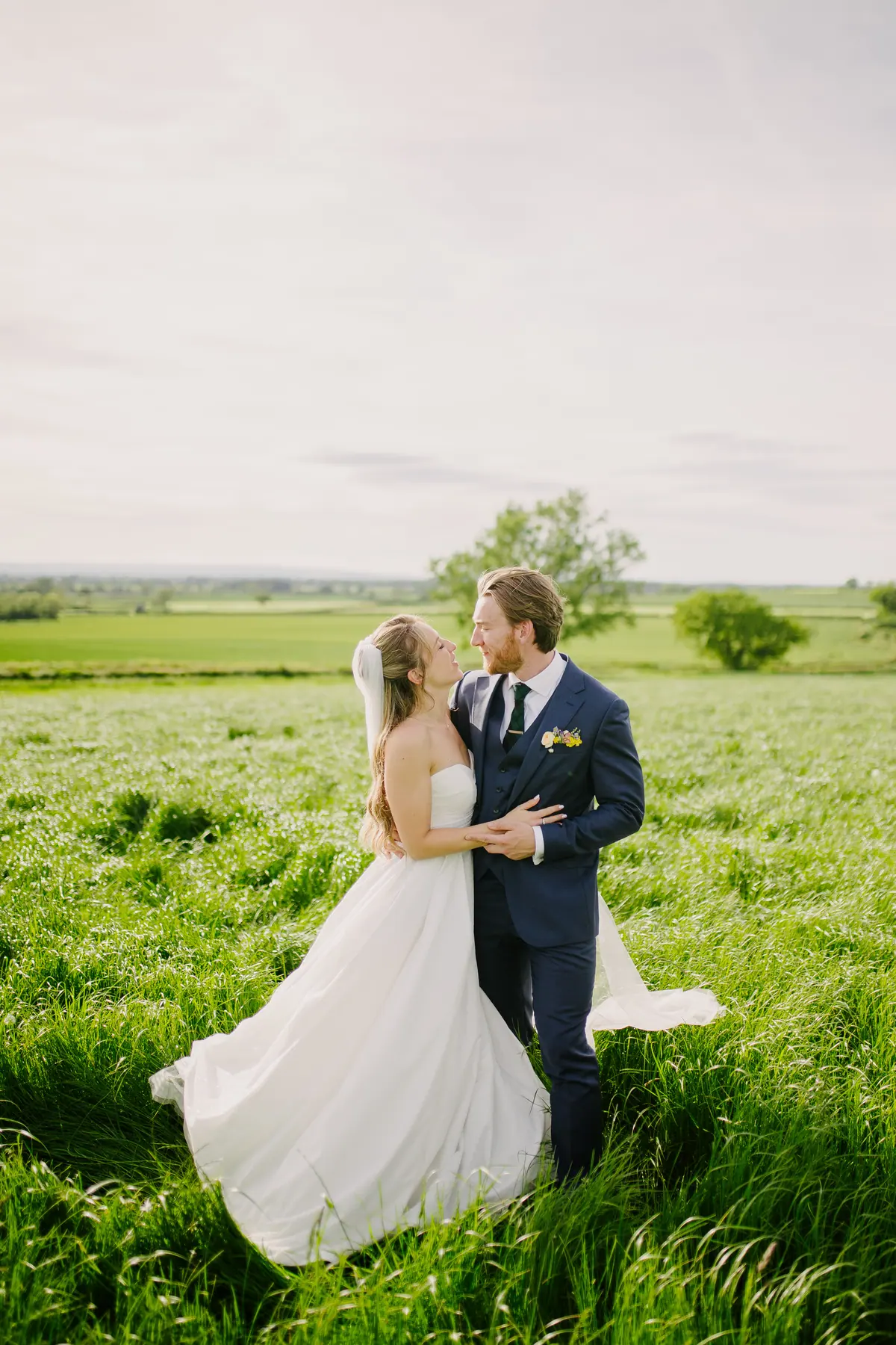 Rachel and Andrew standing together in long green grass beside the fields