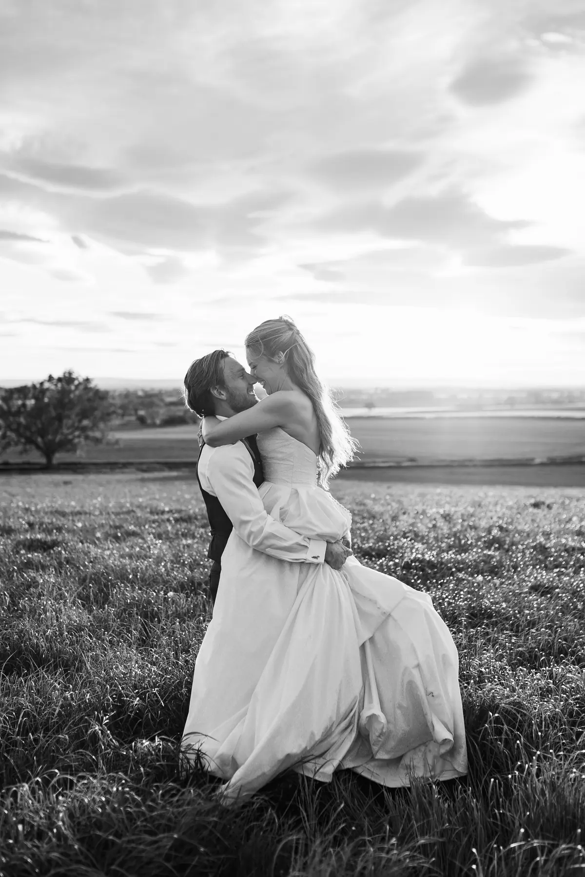 Andrew lifting Rachel in an open field beneath a clouded sky