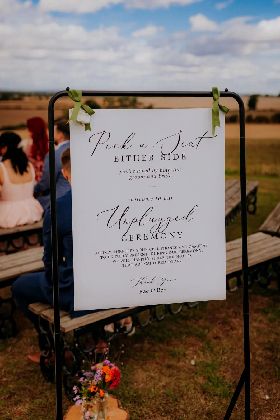 Unplugged ceremony sign beside flowers at the entrance to the benches