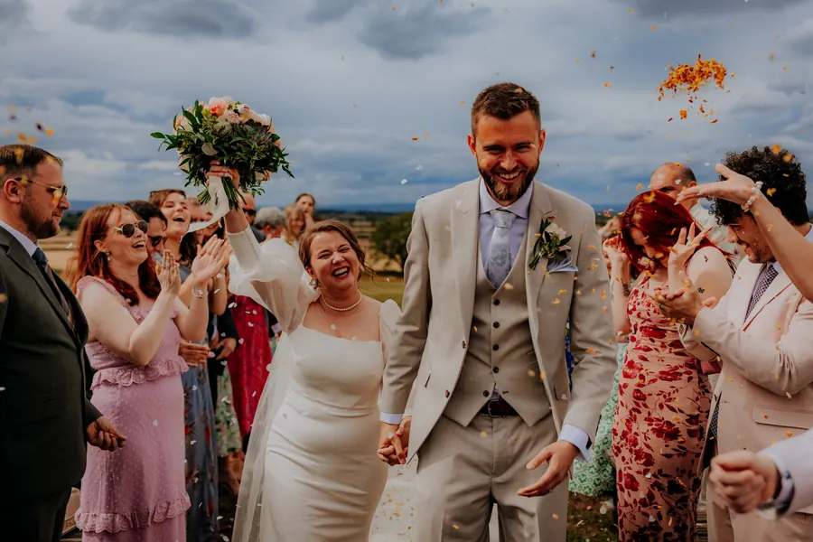The couple walking through confetti with the open fields behind them