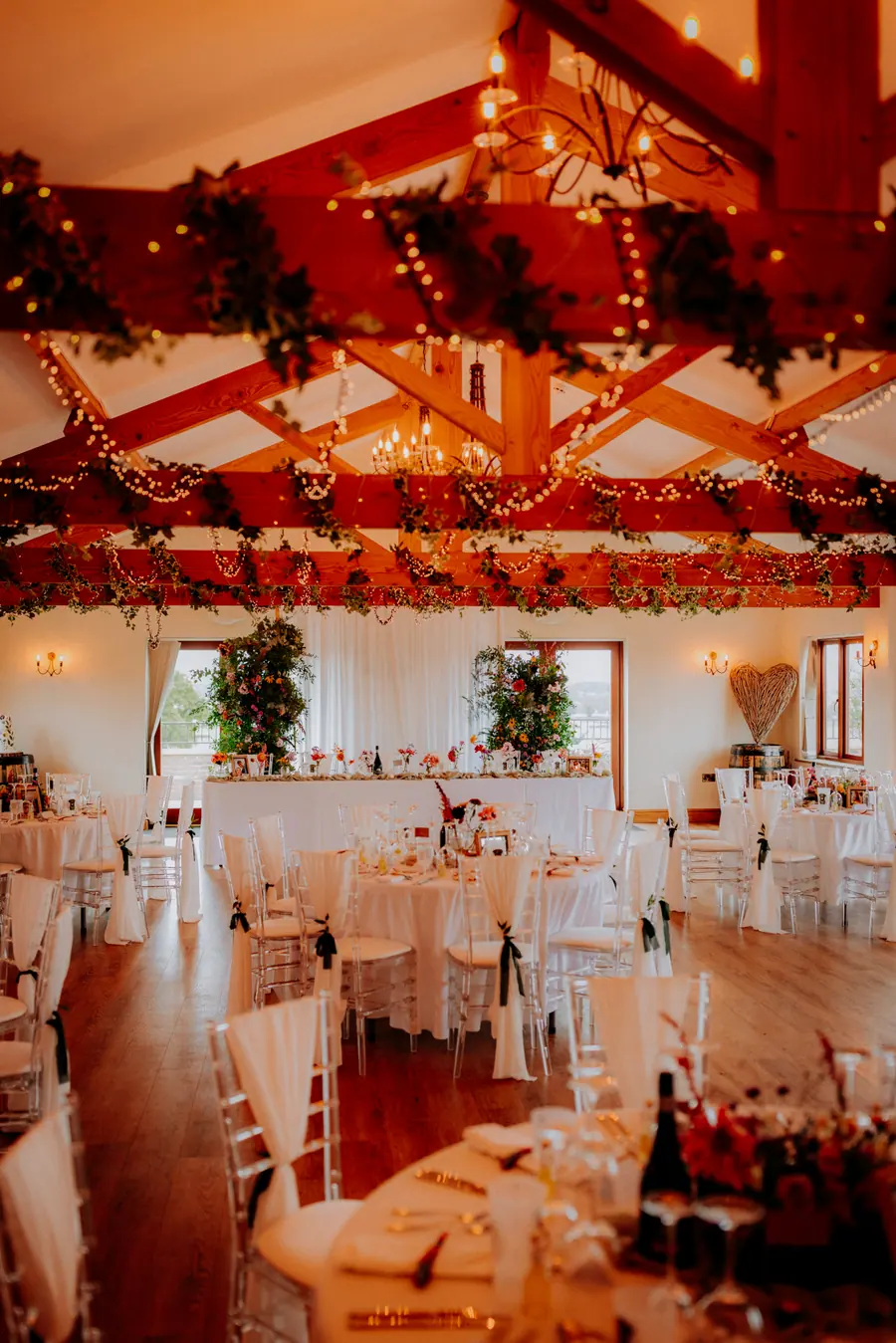 Round Hall tables beneath greenery, red flowers and warm lights