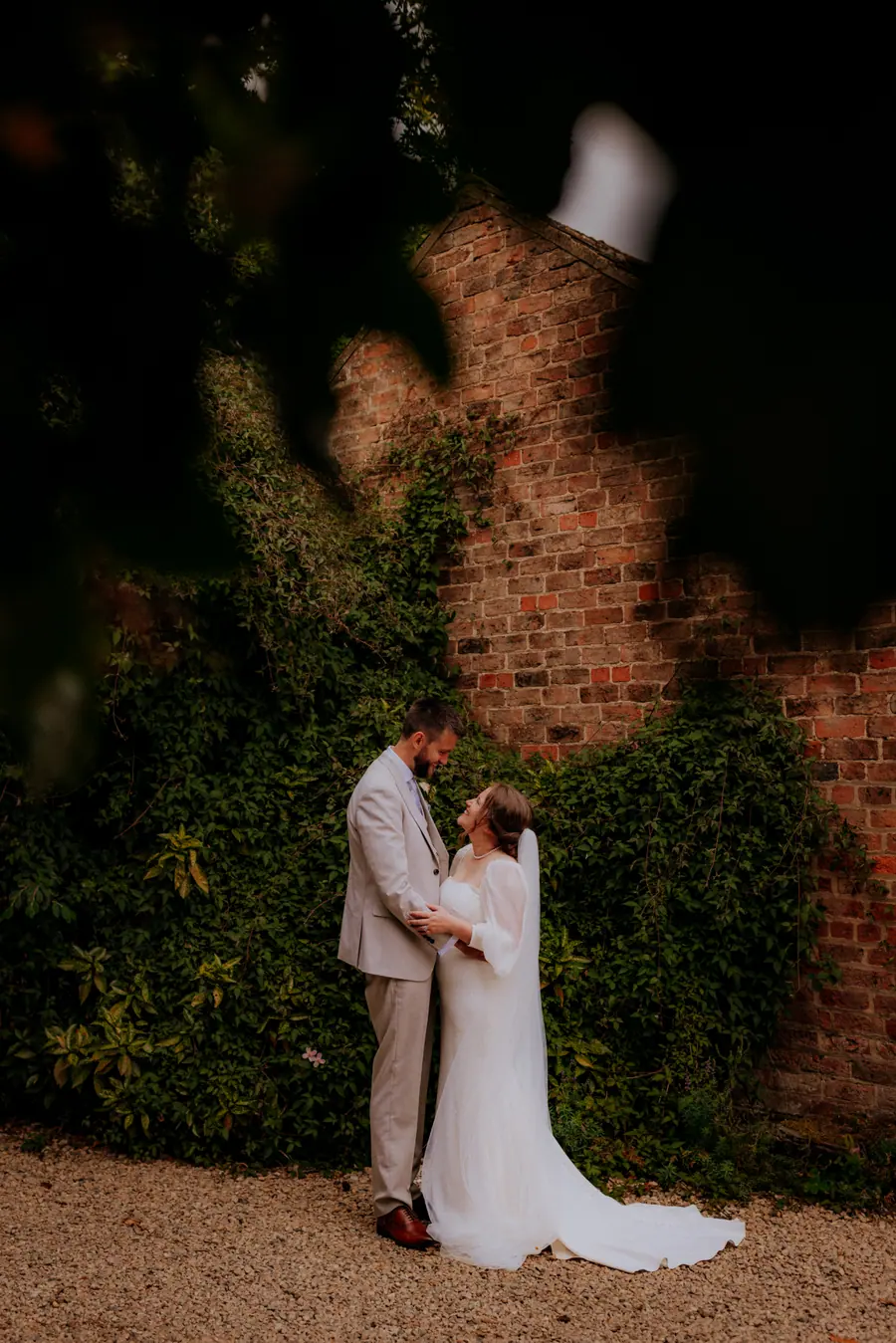 Rae and Ben standing together against ivy-covered brick outside the barns