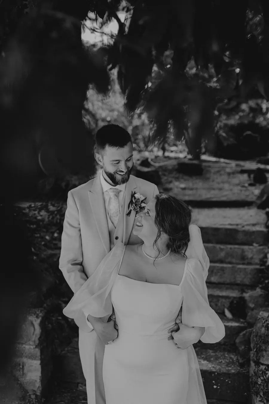 Ben holding Rae beneath trees in a black and white close view