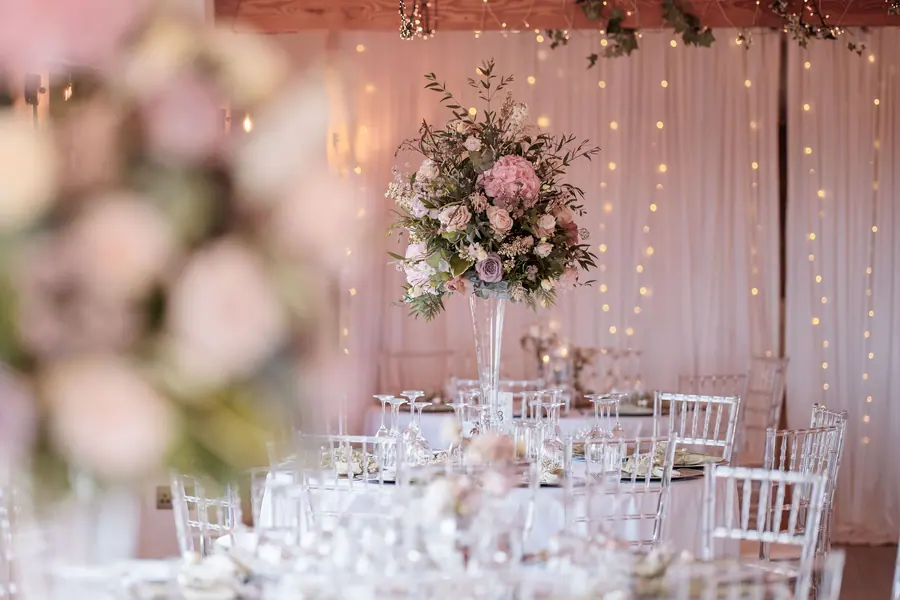 Tall pink and white flowers above clear chairs and laid Hall tables