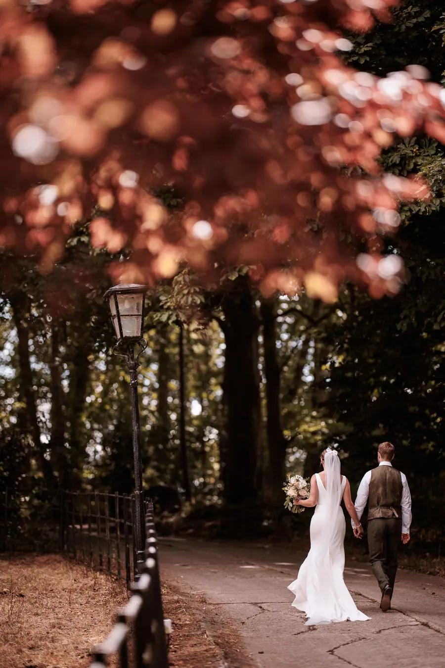 The couple walking away together beneath dark red woodland leaves
