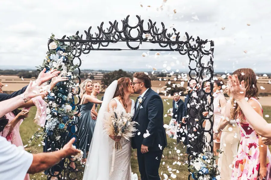 Guests throwing confetti as the couple kiss beneath the horseshoe arch