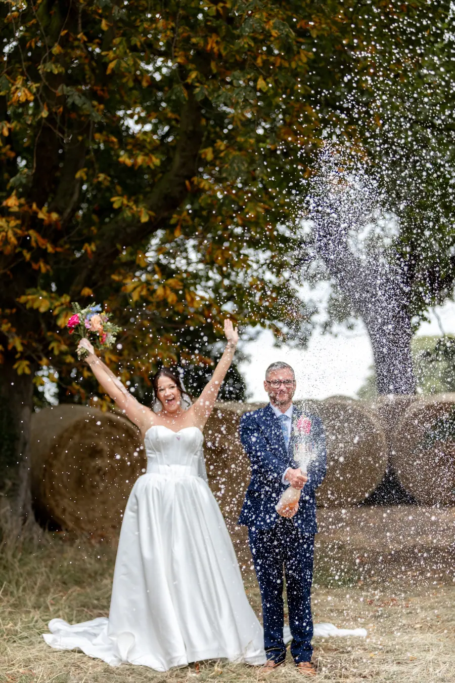 Stacey and Luke standing among hay bales beneath falling confetti