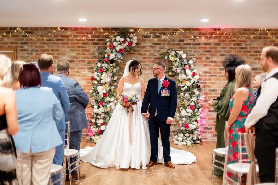 Stacey and Luke standing between floral columns after the indoor ceremony