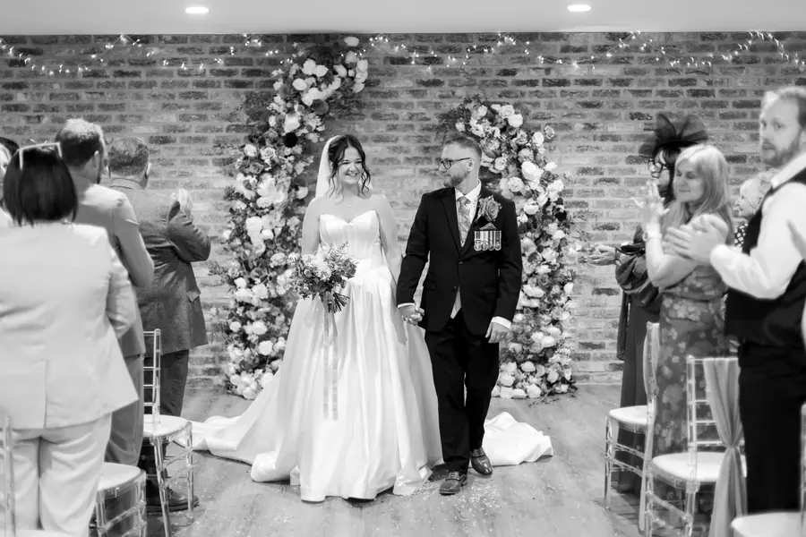 The couple leaving the ceremony aisle together in black and white