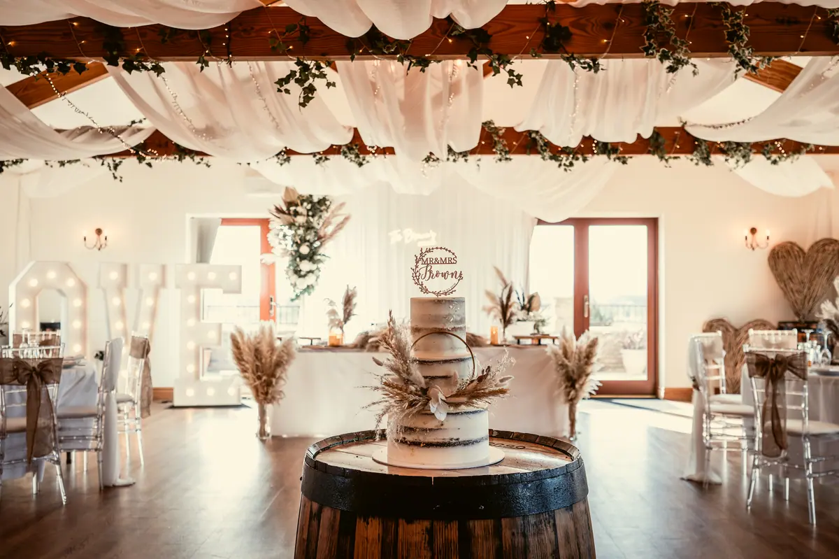 Pale wedding cake displayed on a wooden barrel inside the Hall