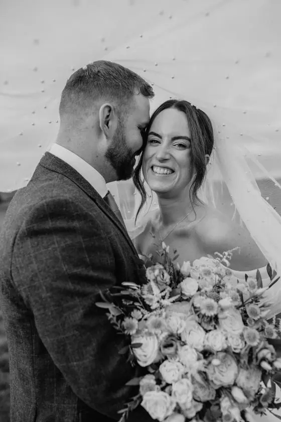 The couple standing close beneath the veil in black and white