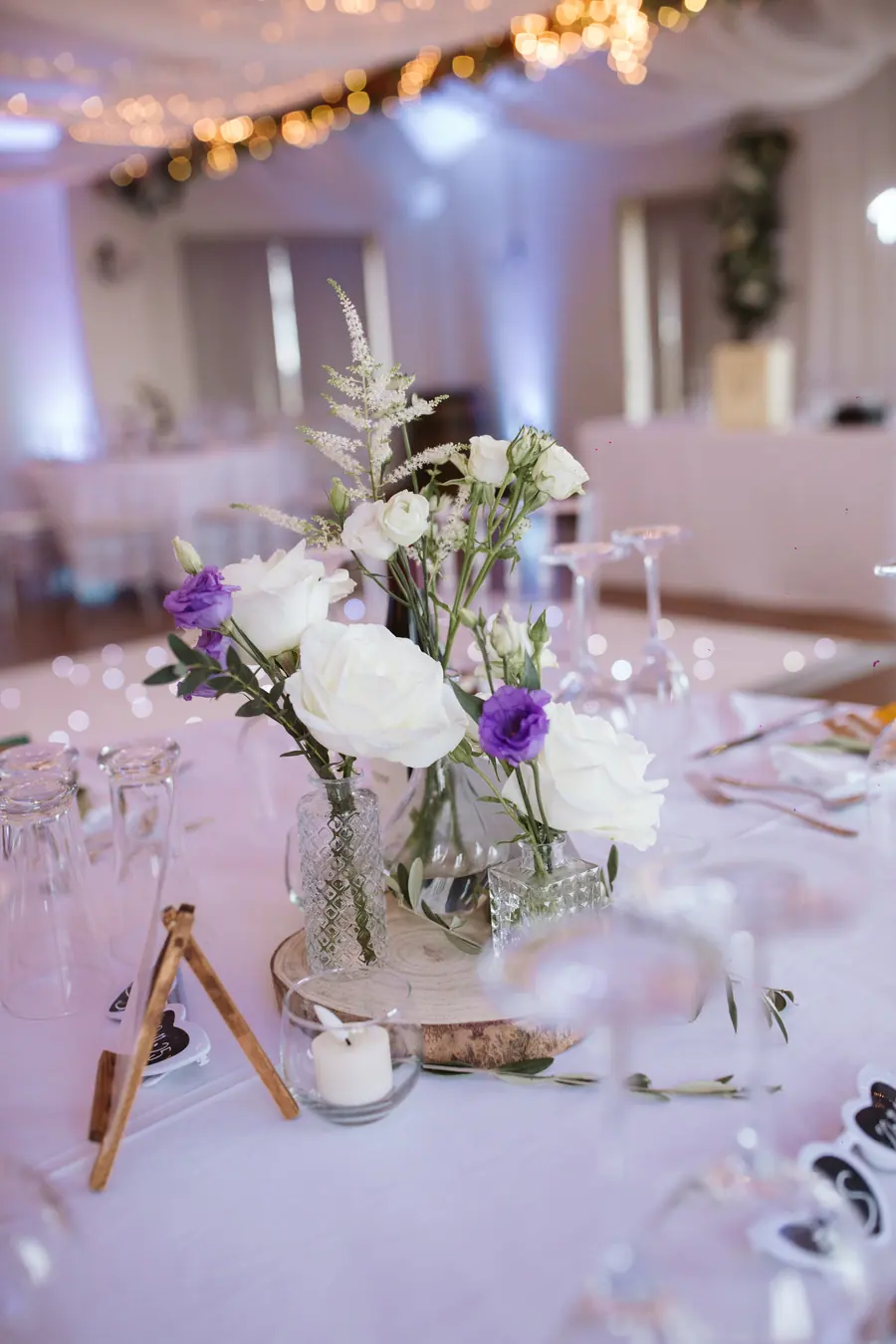 White and purple flowers arranged with candles on a laid table