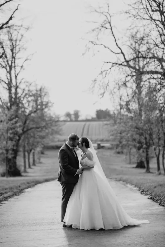 Zoe and Scott standing together on the tree-lined lane in black and white