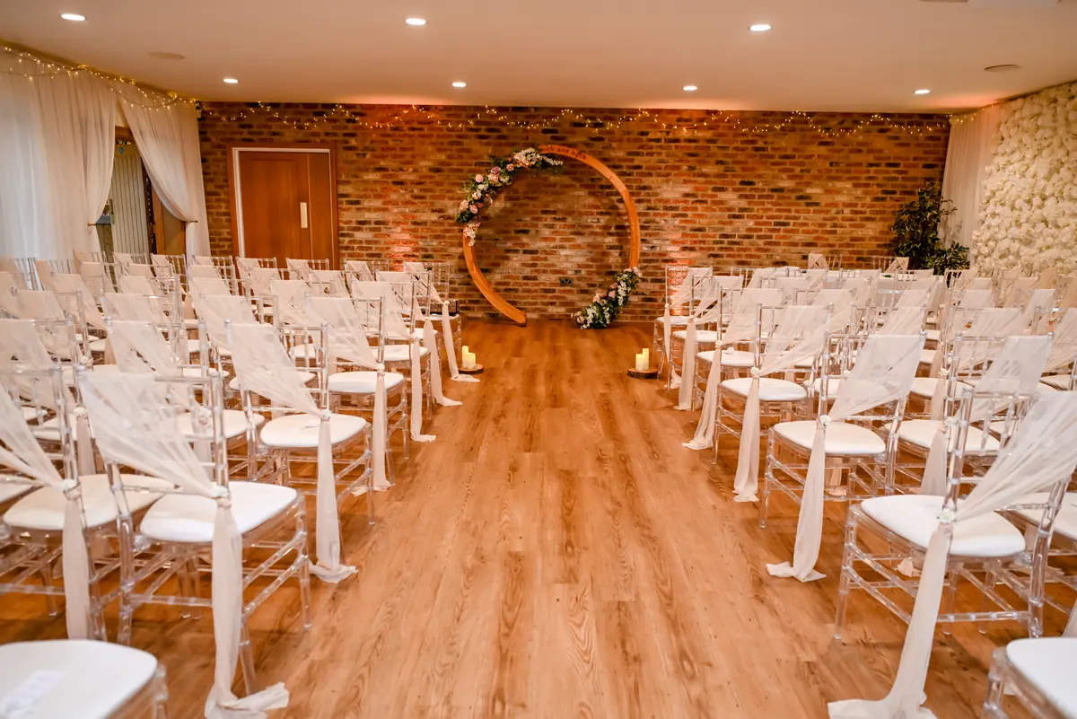 Small Hall ceremony chairs facing a circular floral backdrop on the brick wall