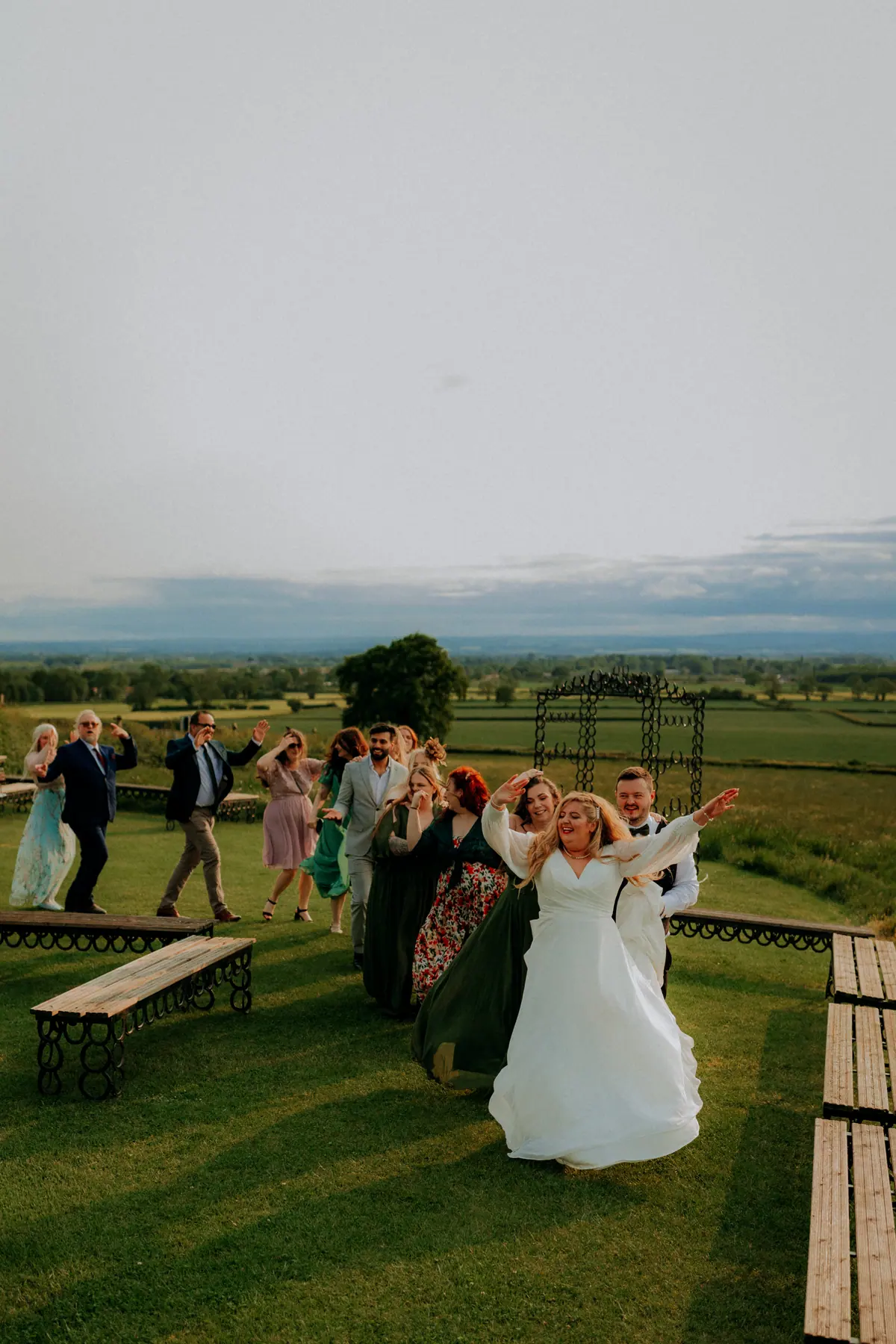 Liv and Luke celebrating with their wedding guests against the North Yorkshire countryside