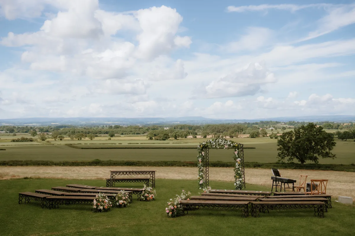 Wooden ceremony benches and a floral arch on the grass overlooking the Yorkshire countryside