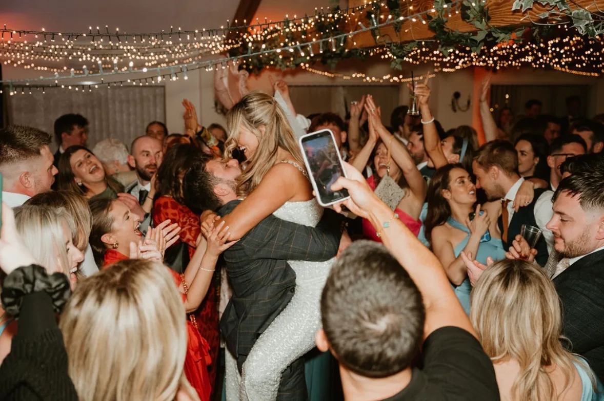 A bride celebrating on the dance floor surrounded by guests