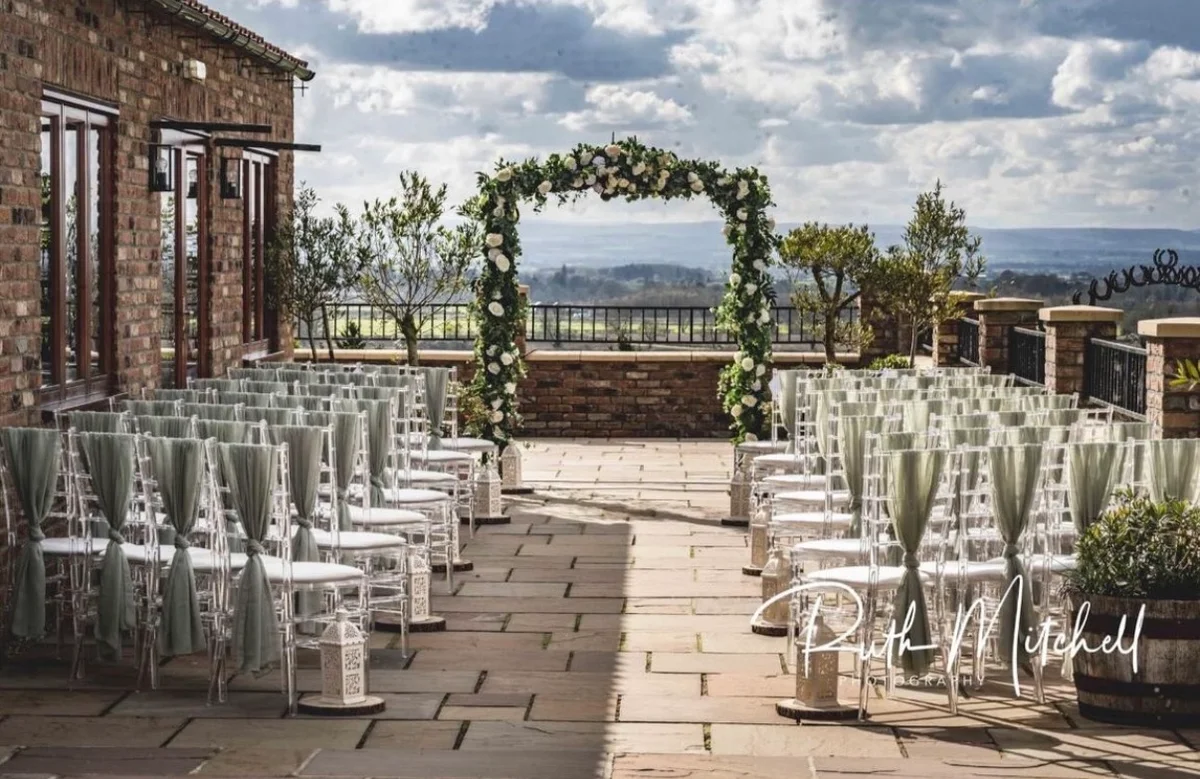 Rows of ceremony chairs facing a floral arch on the Patio, with the Yorkshire countryside beyond
