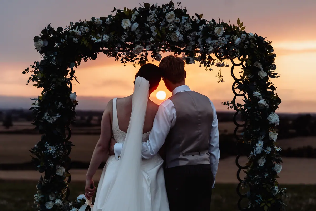 A couple watching the sunset beneath a flower-covered arch at Thief Hall