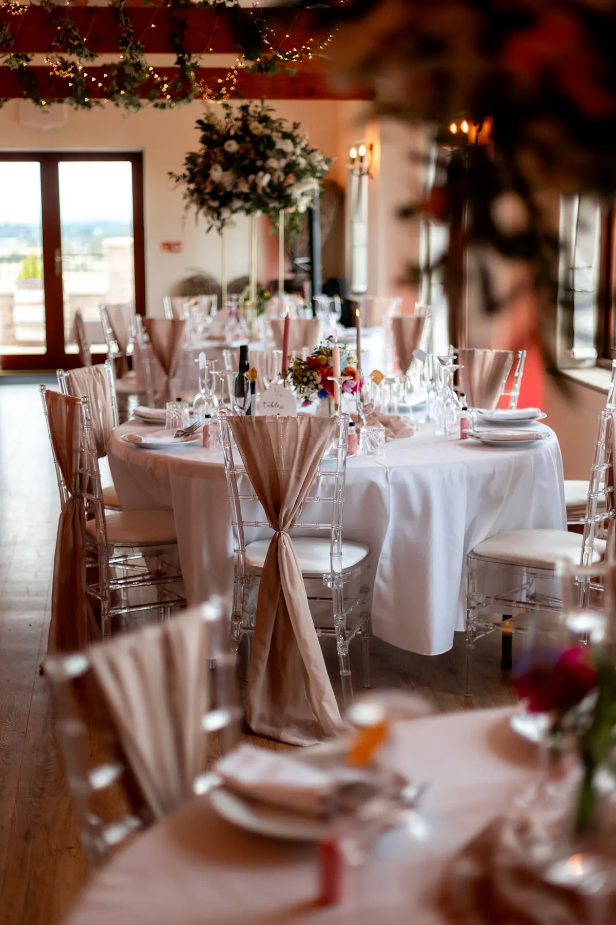 Dressed Hall tables with pink napkins, clear chairs, flowers and glassware