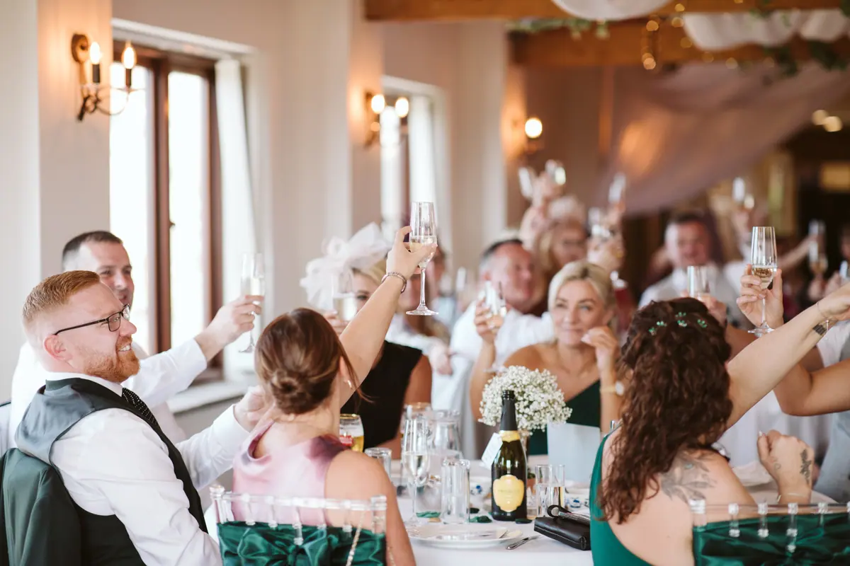 Wedding guests raising glasses together around a table in the Hall